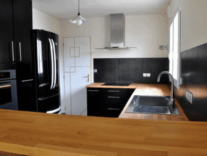 Cuisine moderne et équipée noire et bois. Un frigo rétro noir, hotte inox, plan de travail bois clair et évier intégré.