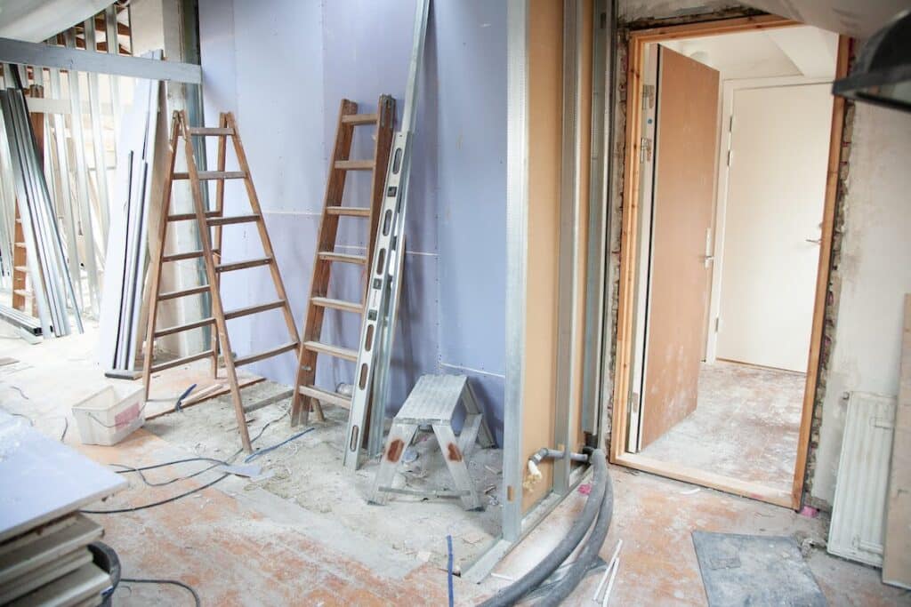 Chantier intérieur en rénovation: murs en plaques de plâtre, montants métalliques, deux échelles, outils et câbles au sol, porte ouverte.