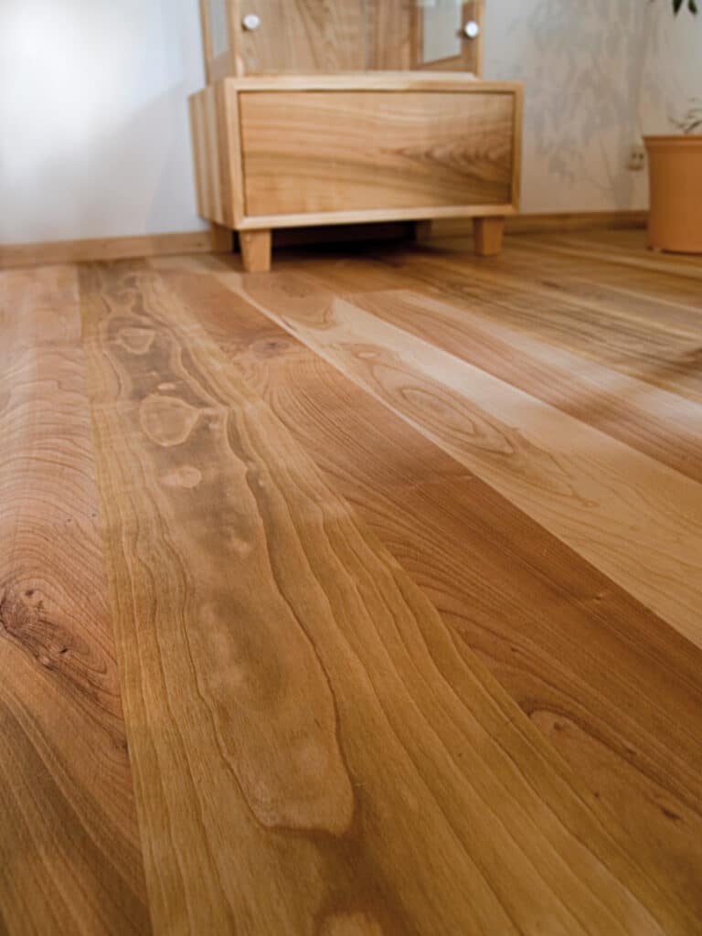 Plancher en bois clair aux motifs naturels s'étendant vers un meuble et une armoire assortis dans un intérieur lumineux.